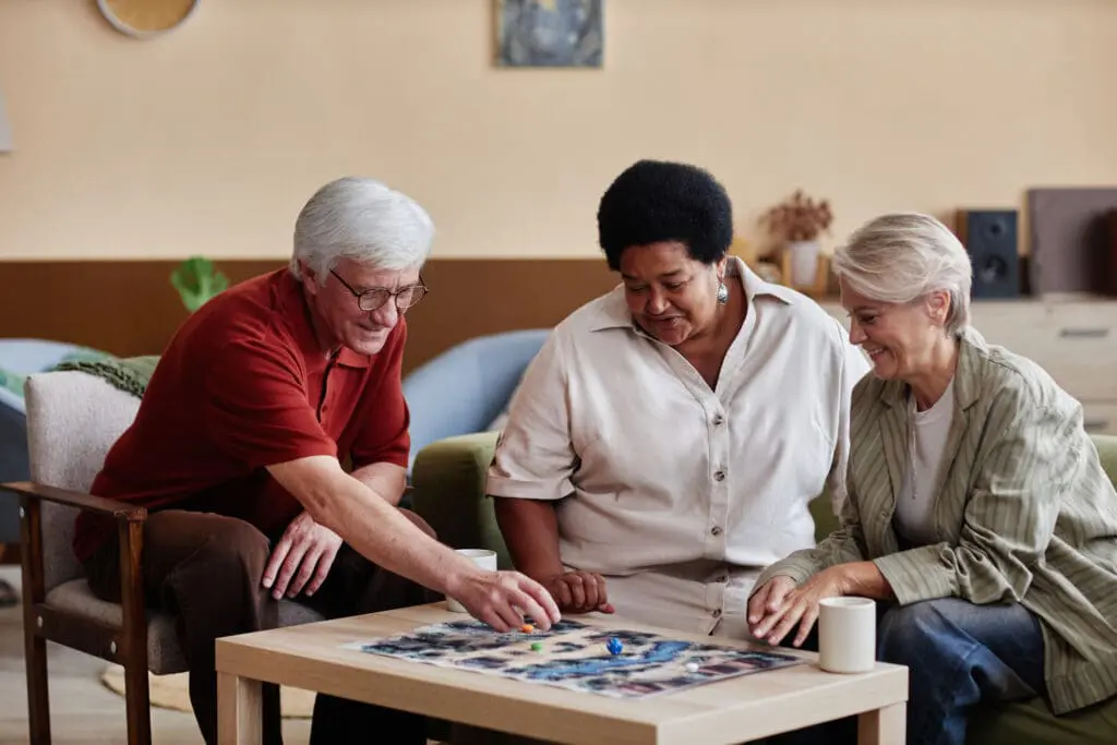 Senior People Playing Board Game in Living Room. This showcases great gifts for someone with Parkinson's disease at Clarendale West End.